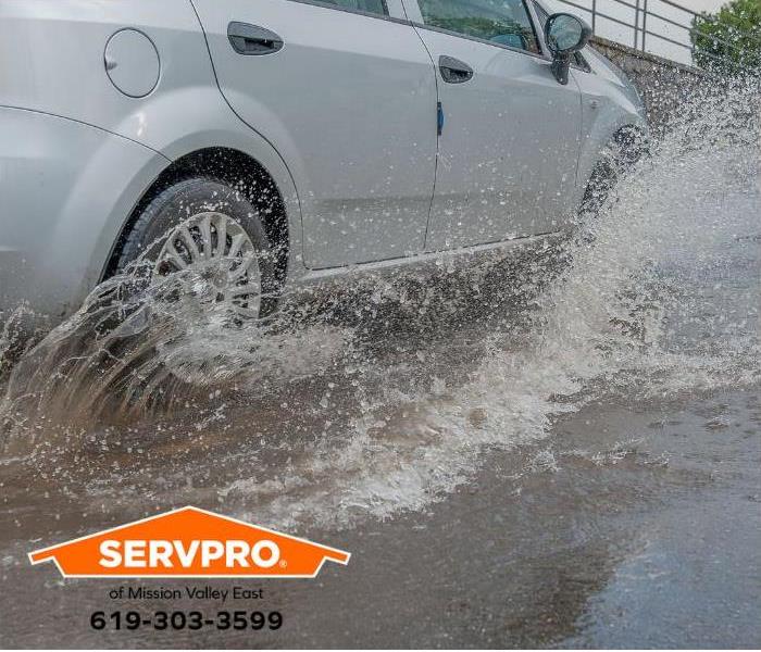 A car drives through a flooded street.